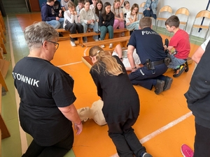 policjanci i ratownik medyczny na spotkaniu z uczniami w szkole. dzieci uczą się na fantomach resuscytacji.