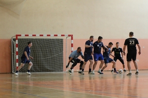 mężczyźni zawodnicy w czasie gry w piłkę nożną na hali sportowej.
