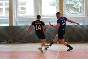 mężczyźni zawodnicy w czasie gry w piłkę nożną na hali sportowej.