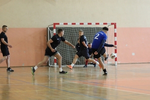 mężczyźni zawodnicy w czasie gry w piłkę nożną na hali sportowej.