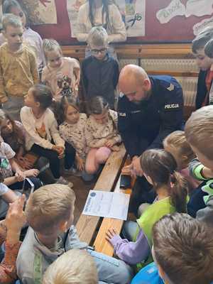 policjant na spotkaniu z uczniami, prowadzi lekcję o ich bezpieczeństwie i rozmawia o pracy policjanta.