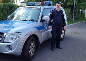 policjant stoi przy radiowozie.