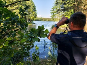 policjant patrzy przez lornetkę , stoi nad akwenem wodnym.