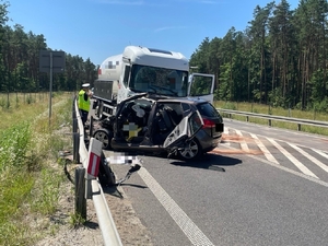 miejsce zdarzenia drogowego. na zdjęciu dwa uszkodzone pojazdy, ciężarówka i osobowy stoją na pasie ruchu, obok policjant.