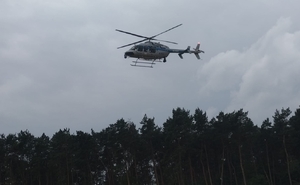 widok policyjnego śmigłowca przeczesującego tereny leśne w akcji poszukiwawczej.