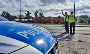 policjanci pełniący służbę w terenie, stoją przy drodze, obok radiowóz. policjant daje sygnał do zatrzymania pojazdu.