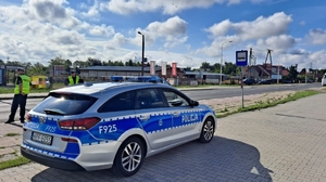 policjanci pełniący służbę w terenie, stoją przy drodze, obok radiowóz.