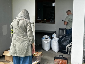 nieumundurowani policjanci w czasie oględzin miejsca ujawnienia kontrabandy, na zdjęciu widoczna posesja oraz worki z nielegalnym towarem.