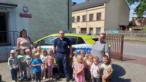 spotkanie policjantów z uczniami. policjant z dziećmi i nauczycielkami stoją przy radiowozie przed budynkiem posterunku policji w Szczercowie.