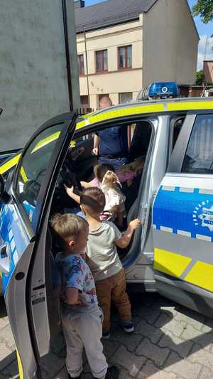 spotkanie policjantów z uczniami. dzieci stoją przy radiowozie przed budynkiem posterunku policji w Szczercowie. policjant pokazuje dzieciom radiowóz.