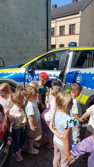 spotkanie policjantów z uczniami. dzieci stoją przy radiowozie przed budynkiem posterunku policji w Szczercowie. policjant pokazuje dzieciom radiowóz.
