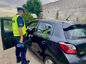 policjant w czasie kontroli kierowcy, stoi przy zatrzymanym do kontroli pojeździe.
