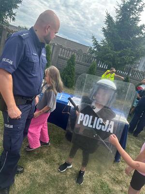 policjant na spotkaniu z dziećmi w ramach akcji bezpieczne wakacje, pokazuje im wyposażanie policjanta do służby.
