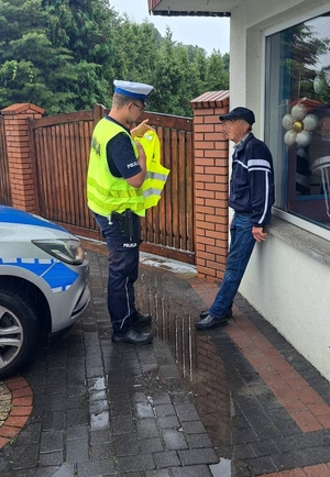 policjant w czasie działań w zakresie bezpieczeństwa ruchu drogowego rozdaje kamizelki odblaskowe pieszym.