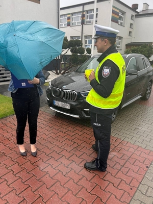 policjant w czasie działań w zakresie bezpieczeństwa ruchu drogowego rozdaje kamizelki odblaskowe pieszym.