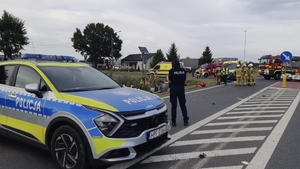 Na zdjęciu policyjny radiowóz i policjantka na miejscu zdarzenia drogowego.