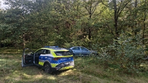 miejsce porzucenia pojazdu. na zdjęciu pojazd osobowy przy nim radiowóz. teren leśny