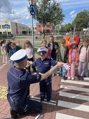 policjant pokazuje chłopcu na czym polega praca policjanta ruchu drogowego w obrębie przejścia dl pieszych, policjanci uczą dzieci prawidłowych zachowań na przejściu dla pieszych.
