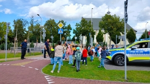 dwóch policjantów oraz radiowóz policyjny na terenie miasteczka ruchu drogowego. Policjanci prowadza z dziećmi lekcję o bezpieczeństwie w ruchu drogowym.