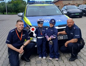 dwóch policjantów i dwóch chłopców w przebraniu policjanta, dalej radiowóz.