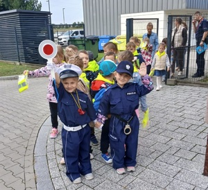 grupa przedszkolaków, wyposażona w kamizelki odblaskowe. dzieci wychodzą z terenu posterunku, gdzie policjant prowadził z nimi lekcję o bezpieczeństwie.