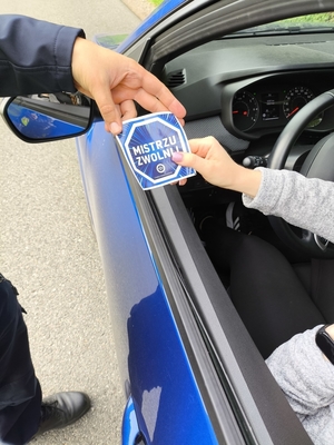 policjantka wręcza kierowcy ulotkę mistrzu zwolnij.