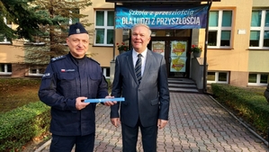 zdjęcie z akcji Odblaski ratują życie, która była wspólną akcją Policji i Starostwa Powiatowego w ramach kampanii „Bezpieczna droga do szkoły”. Na zdjęciu Komendant i Starosta Bełchatowski, stoją przed budynkiem szkoły.