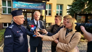 zdjęcie z akcji Odblaski ratują życie, która była wspólną akcją Policji i Starostwa Powiatowego w ramach kampanii „Bezpieczna droga do szkoły”. Na zdjęciu Komendant i Starosta Bełchatowski, stoją przed budynkiem szkoły. komendant i starosta w czasie udzielania wywiadu mediom.