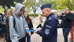 zdjęcie z akcji Odblaski ratują życie, która była wspólną akcją Policji i Starostwa Powiatowego w ramach kampanii „Bezpieczna droga do szkoły”. Na zdjęciu Komendant i Starosta Bełchatowski,  przed budynkiem szkoły. Komendant rozdaje uczniom odblaski.