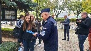 zdjęcie z akcji Odblaski ratują życie, która była wspólną akcją Policji i Starostwa Powiatowego w ramach kampanii „Bezpieczna droga do szkoły”. Na zdjęciu Komendant. Przed budynkiem szkoły Komendant rozdaje uczniom odblaski.