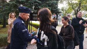 zdjęcie z akcji Odblaski ratują życie, która była wspólną akcją Policji i Starostwa Powiatowego w ramach kampanii „Bezpieczna droga do szkoły”. Na zdjęciu Komendant. Przed budynkiem szkoły Komendant rozdaje uczniom odblaski.