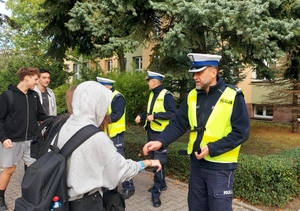 policjanci ruchu drogowego przed szkolą rozdają uczniom elementy odblaskowe.