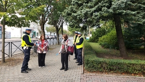 policjanci ruchu drogowego przed szkolą rozdają uczniom elementy odblaskowe.