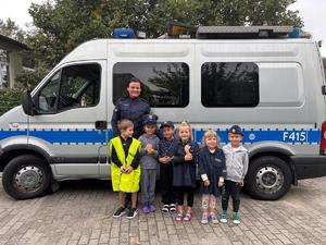 policjant na spotkaniu z uczniami , stoją przy radiowozie.
