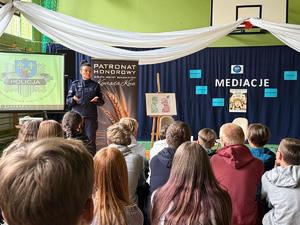 Policjantka stoi przed grupą siedzących dzieci.
