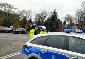 Radiowóz i dwie policjantki na tle cmentarza.