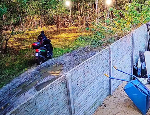 Mężczyzna jedzie skuterem za ogrodzeniem.