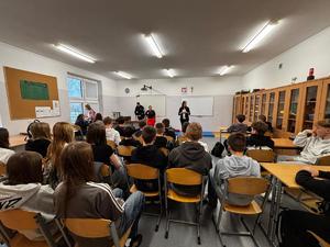 Policjant stojący przed uczniami, które siedzą w ławkach.