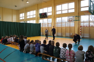 Komendant wraz z wójtem stoją przed dziećmi na sali gimnastycznej.