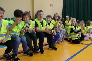 Dzieci siedzą w kamizelkach odblaskowych.
