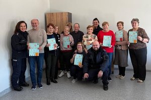 Grupa seniorów pozuje do zdjęcia z policjantami trzymając w ręku ulotki.