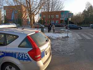 Radiowóz i w tle policjantki rozmawiają z seniorką.