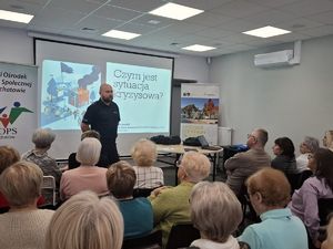 Policjant stoi przed grupą ludzi na tle prezentacji.