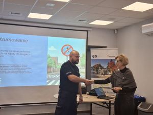 Policjant stoi przed grupą ludzi i wita się z kobietą.