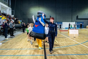 Policjantka z maskotką Komisarzem Błyskiem wprowadza zawodników na halę.