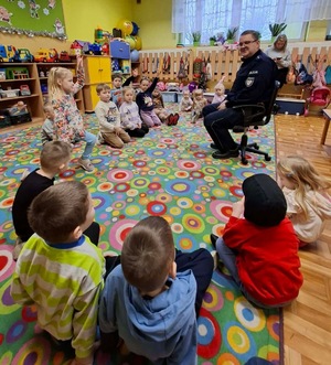 Policjant siedzi przed grupą dzieci.