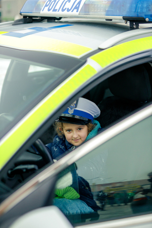 Dziewczynka siedzi za kierownicą radiowozu w białej czapce policyjnej.
