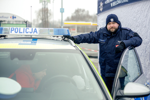 Policjant przy otwartych drzwiach radiowozu.