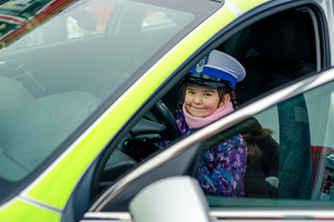 Dziewczynka w czapce policyjnej za kierownicą radiowozu.