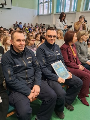 Dwóch policjantów siedzą z publicznością.